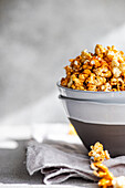 A bowl of sweet caramel popcorn on a grey napkin, the background is softly blurred.