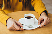 A cosy scene with a woman holding a cup of coffee on a wooden table She is wearing a warm yellow jumper, which creates a cosy and inviting atmosphere Perfect for coffee-related themes