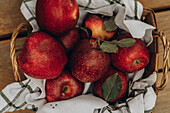 Top view of a rustic basket filled with juicy red apples, accentuated by green leaves and a striped cloth depicting a fresh and organic scene.