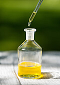 Eine Pipette, die Öl in eine kleine Glasflasche abgibt, vor einem sanft fokussierten grünen Hintergrund. Ideal zur Illustration von Themen im Zusammenhang mit Wellness, Aromatherapie oder Naturprodukten.