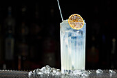 A refreshing gin fizz cocktail, served in a tall glass, garnished with a dried citrus slice The drink is surrounded by ice cubes, giving it a touch of elegance and coolness