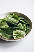 Fresh green spinach leaves in a ceramic bowl from above on a white background. The bright spinach leaves offer a natural, healthy food theme, ideal for culinary purposes.