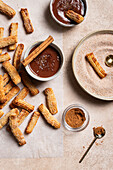 Top view of homemade churros generously dusted with sugar and cinnamon, accompanied by a rich chocolate sauce and a pinch of sea salt, all on a textured ceramic background that creates an atmospheric ambience.