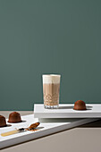 A glass of coffee with creamy milk foam, surrounded by brown sugar and coffee capsules, against a minimalist backdrop - perfect for caffeine lovers and cosy moments