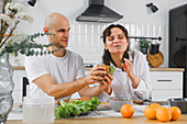 A happy blind couple enjoy a healthy meal in a modern kitchen. The scene reflects warmth and connection as they eat sandwiches together surrounded by fresh ingredients.