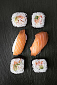 An elegant sushi presentation with nigiri of fresh salmon and sushi rolls with crab, avocado, salmon and rice, beautifully arranged on a black slate surface