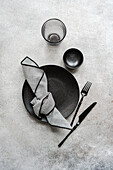 A sophisticated black and white table setting with textured plates, stylish glasses, striped napkin and simple cutlery. Perfect for a modern dinner setting.