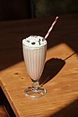 A delicious vanilla milkshake with whipped cream and chocolate chips is elegantly served in a vintage glass A white and red striped straw adds a playful touch