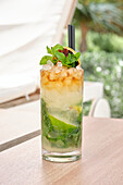 A tangy mojito cocktail stands on a wooden table, garnished with fresh mint leaves and lime slices. The icy attraction and bright colours of the drink underline its refreshing appeal.