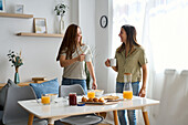 A lesbian couple having a cosy breakfast at home They smile warmly at each other, holding coffee cups, surrounded by a bright and welcoming atmosphere