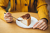 A person in a cosy yellow jumper enjoys a piece of chocolate cake while leaning on a fork. The scene radiates warmth and delicious pleasure.