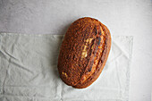 View from above of a freshly baked sourdough bread with a crispy crust resting on a white linen cloth, a perfect example of traditional home baking.