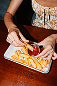 Eine Frau taucht knusprige Kartoffelspalten in einen Becher mit reichlich Ketchup. Dieser köstliche Snack wird auf einem Tablett serviert und eignet sich perfekt für eine zwanglose Mahlzeit oder einen schnellen Imbiss.