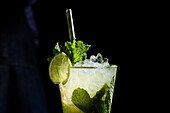 A lively mojito cocktail, garnished with fresh mint leaves and a slice of lime, set against a dark background The ice cubes give it a refreshing flavour and make it an ideal summer drink