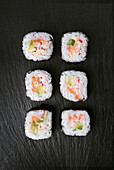 A series of sushi rolls elegantly arranged on a dark stone background provides a vibrant contrast. Ideal for themes of cuisine, Asian culture and culinary arts.