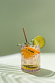 An image of a lively and refreshing summer cocktail on a calming green background, garnished with a slice of lime and a sprig of mint.