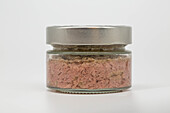 Close-up of a glass jar filled with creamy tuna pâté and sealed with a metal lid against a light-coloured background. The image emphasises the texture and simplicity of food packaging.