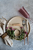A beautifully arranged autumn table with a beige plate, elegant cutlery, pink flowers and a glass on a textured surface - ideal for seasonal dining themes