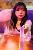 An Asian Gen Z girl enjoys the atmosphere of an arcade and holds candyfloss in her hand while playing a game.