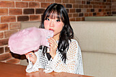 An Asian Gen Z girl enjoys candyfloss in a lively arcade Her cheerful facial expression and casual outfit convey fun and youthfulness