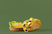 A vibrant taco filled with fresh vegetables, chicken and cheese, complemented by lemon slices and lettuce against a green background, presenting a healthy meal
