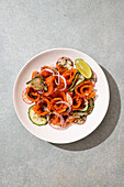 A vibrant salad with smoked salmon, cucumber slices, radishes, onions and dill, artfully arranged on a plate with a slice of lime, provides a refreshing summer flavour.