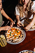 Two people share a Margherita pizza topped with mozzarella, basil and tomato sauce. A refreshing lemonade is on the table and emphasises the friendly dining experience.
