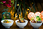 Trio of gourmet dishes, tempura mushrooms in curry sauce, aubergine stew with rice and roast beef with vegetables, pear and sesame seeds The festive setting is decorated with warm lighting and floral décor