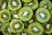 A close-up of several fresh kiwi slices, showing their bright green colour and characteristic seed pattern, highlighting their juicy and refreshing texture.