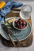 A tasteful arrangement of Greek grilled olives on a ceramic plate, accompanied by a glass, rustic utensils and textured bed linen. The scene captures a balance of elegance and tradition and is perfect for culinary themes.