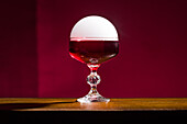 An eye-catching Negroni cocktail, garnished with a smoke bell, set against a deep red background. The elegant glass and sophisticated presentation are perfect for emphasising the creative mixology