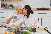 A blind couple share a loving moment in their modern kitchen, surrounded by fresh vegetables and coffee. The scene captures warmth and authenticity in a cosy home.