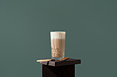 Elegant glass of coffee with creamy milk, served on a dark wooden surface A spoon with brown sugar lies next to it, creating a warm and inviting atmosphere
