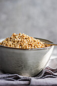 A bowl filled with chopped hazelnuts rests on a grey textured napkin, accompanied by an antique spoon.