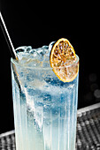 A refreshing gin fizz cocktail, served in a tall glass, garnished with a dried citrus slice The drink is surrounded by ice cubes, giving it a touch of elegance and coolness