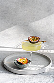 A stylish cocktail of tonic, gin and passion fruit juice, served in an elegant glass. A halved passion fruit provides a decorative and exotic accent on a silver tray in subdued lighting.