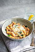 Cavatappi pasta with grated Parmesan cheese, fresh spinach and tangy tomato sauce, served in a ceramic bowl. Served with a refreshing glass of water with lemon on a soft cloth napkin.