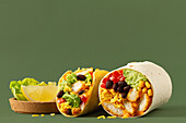 A delicious taco and burrito cut in half, featuring a colourful mix of chicken, black beans, corn, cheese and guacamole on a textured green background A slice of lemon and lettuce are also provided