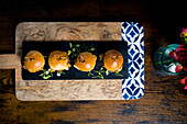 Top view of four gourmet mini burgers with pulled pork and cabbage, served on a black slate with fresh greens, arranged on a rustic wooden tray Perfect for starters or finger food