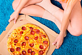 A person in comfortable clothes sits on a fluffy blue carpet and enjoys a delicious pepperoni pizza The warm ambience captures a moment of cosy relaxation at home