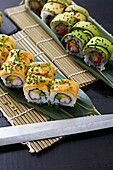 Various sushi rolls, elegantly arranged on a bamboo mat, topped with avocado and seafood and garnished with sesame seeds and green onions.