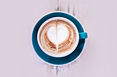 A beautifully designed cappuccino with heart-shaped foam in a bright blue cup. The artistic latte art adds a touch of love and creativity to your coffee experience.