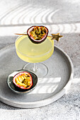 Elegant gin and tonic cocktail mixed with passion fruit juice, garnished with a fresh passion fruit half, presented on a stylish grey tray in subdued lighting.