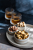 A selection of spiced cognac cocktails with cinnamon and star anise, accompanied by various nuts such as almonds, peanuts and hazelnuts, elegantly presented on a textured grey ceramic surface.