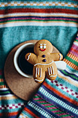 A charming gingerbread man rests on a coffee cup against a vibrant, striped fabric background - a perfect, cosy, festive and warm holiday scene