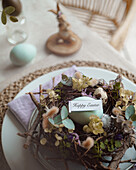 Top view of an elegantly laid Easter table with naturally coloured eggs in a decorative nest with spring flowers and a sign saying Happy Easter.