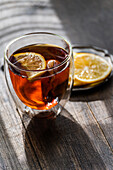 A warm glass of English tea with a slice of lemon, presented on a rustic wooden table, captures the essence of a cosy afternoon.