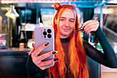 A woman with vibrant hair takes a selfie while visiting an Asian food market, playfully holding chopsticks The scene is colourful and vibrant, capturing the essence of travel and cultural immersion