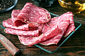 Thin slices of Spanish salami are arranged on a glass plate on a rustic wooden table. The marbled meat displays rich textures and colours and offers a tasty visual treat.