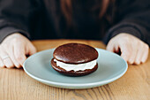 A delicious whoopie pie with a rich chocolate coating and creamy filling is ready to eat on a ceramic plate. Perfect for dessert lovers and gourmets.